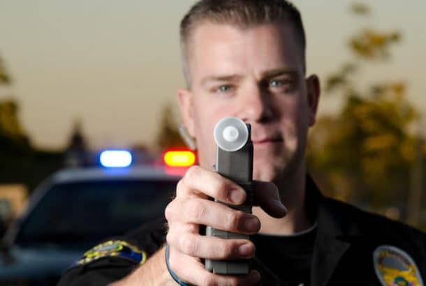 警察持有怀疑的呼吸测试机器吹进一辆警车在后台。